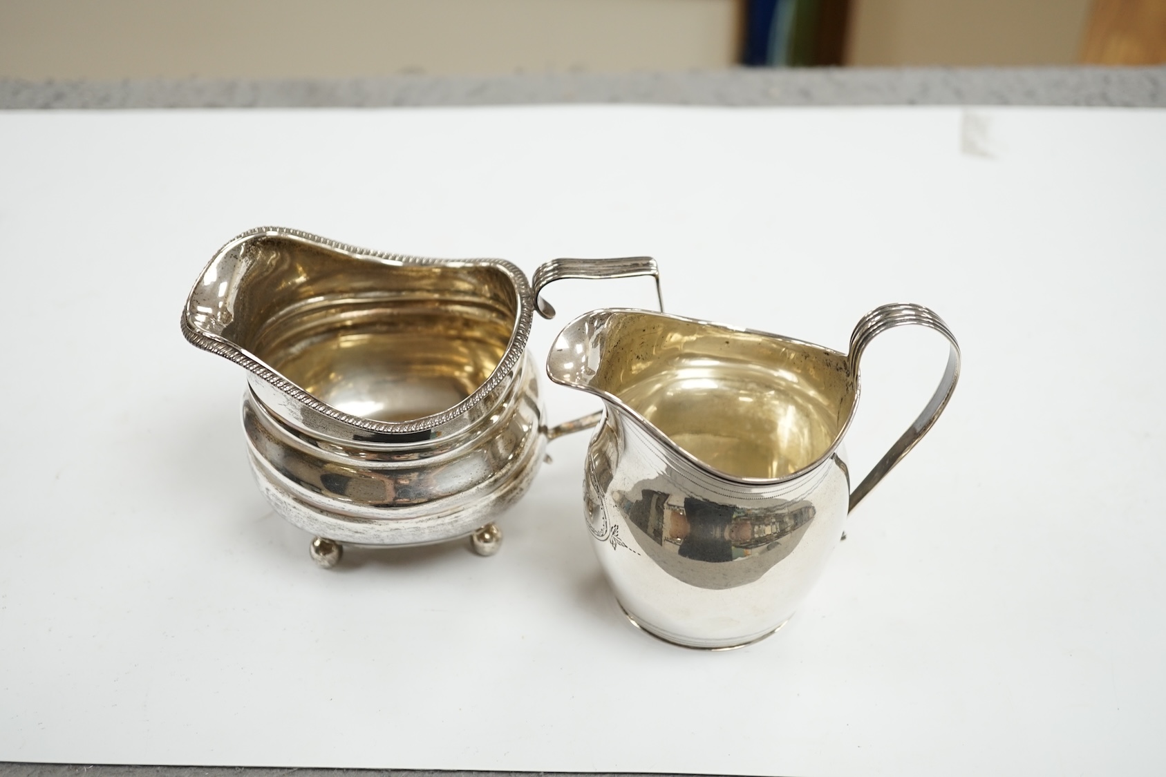 A George III silver helmet shaped cream jug, London, 1806, 10.2cm, together with another George III silver cream jug(repair). Condition - poor to fair